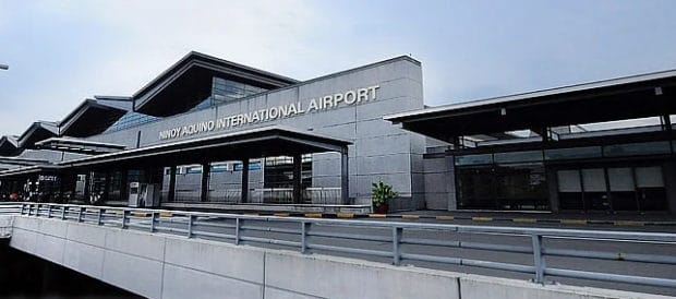 Exterior view of Ninoy Aquino International Airport with modern, angular architecture, large glass windows, and Ninoy Aquino International Airport signage on the building under a partly cloudy sky.