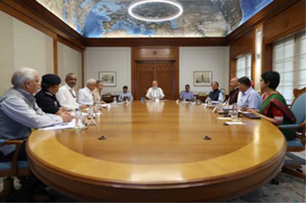 A group of officials seated around a large oval conference table in a formal meeting room with a world map on the ceiling and a circular light overhead.