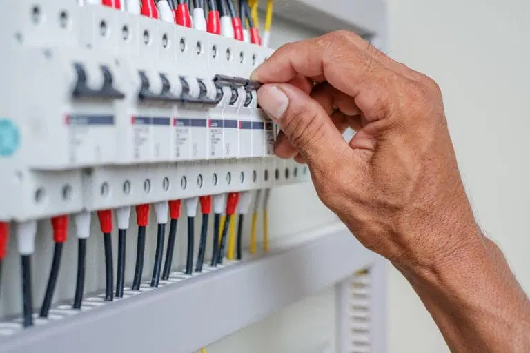 A hand is flipping a switch on an electrical circuit breaker panel with multiple switches, wires, and labels visible during Power Quality Testing.