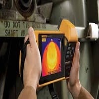 A person holds a thermal camera displaying a heat map, inspecting machinery with the text DO NOT TIE... visible on the metal surface in the background.