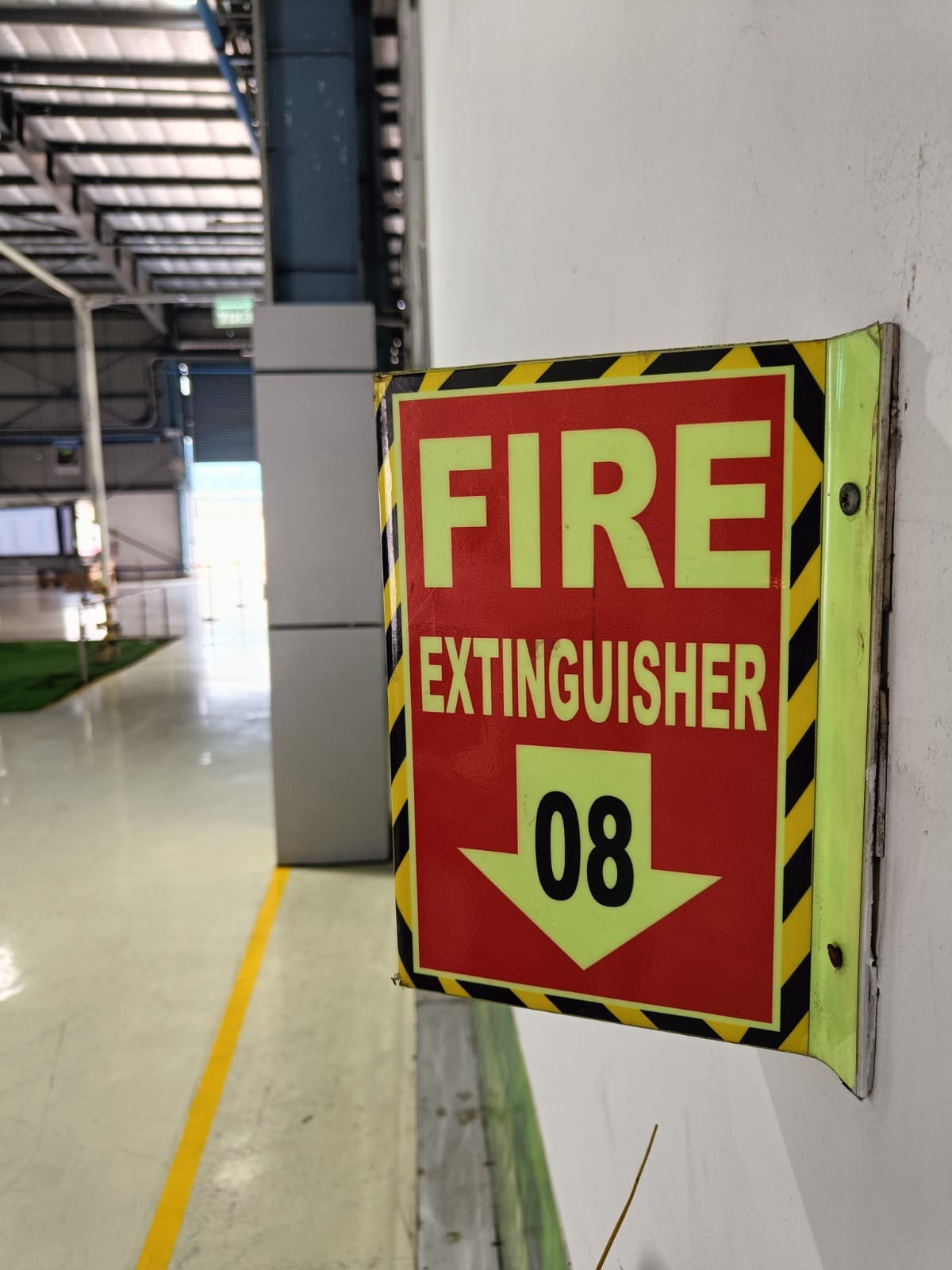A red and yellow sign on a wall reads FIRE EXTINGUISHER 08 with a downward arrow, marking the extinguishers spot, ideal for quick identification during a fire risk assessment in an industrial building.