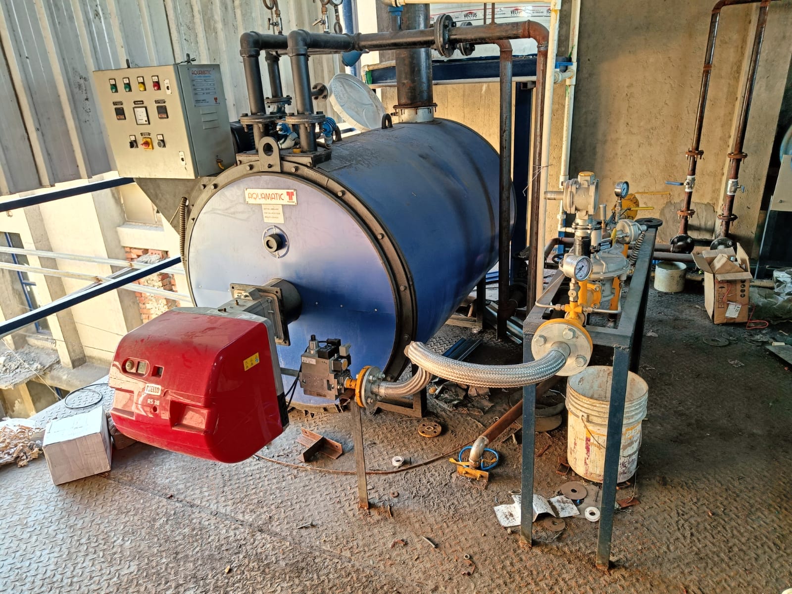 Large horizontal blue industrial boiler with a red burner unit, control panel on the left, and attached pipes and gauges, situated in a factory; ideal for facilities prioritizing workplace safety and routine safety inspections.