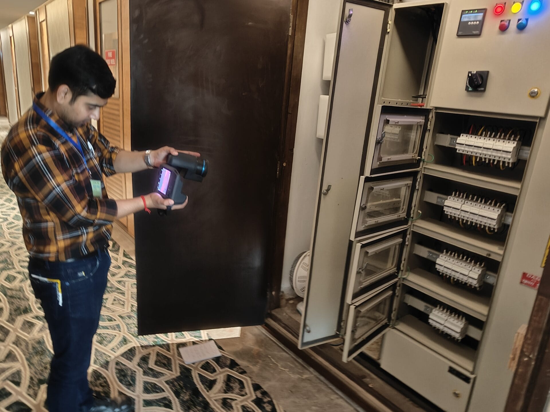 Electrical thermography inspection, scanning an open panel with multiple wiring components in a hallway. The panel is mounted against the wall.