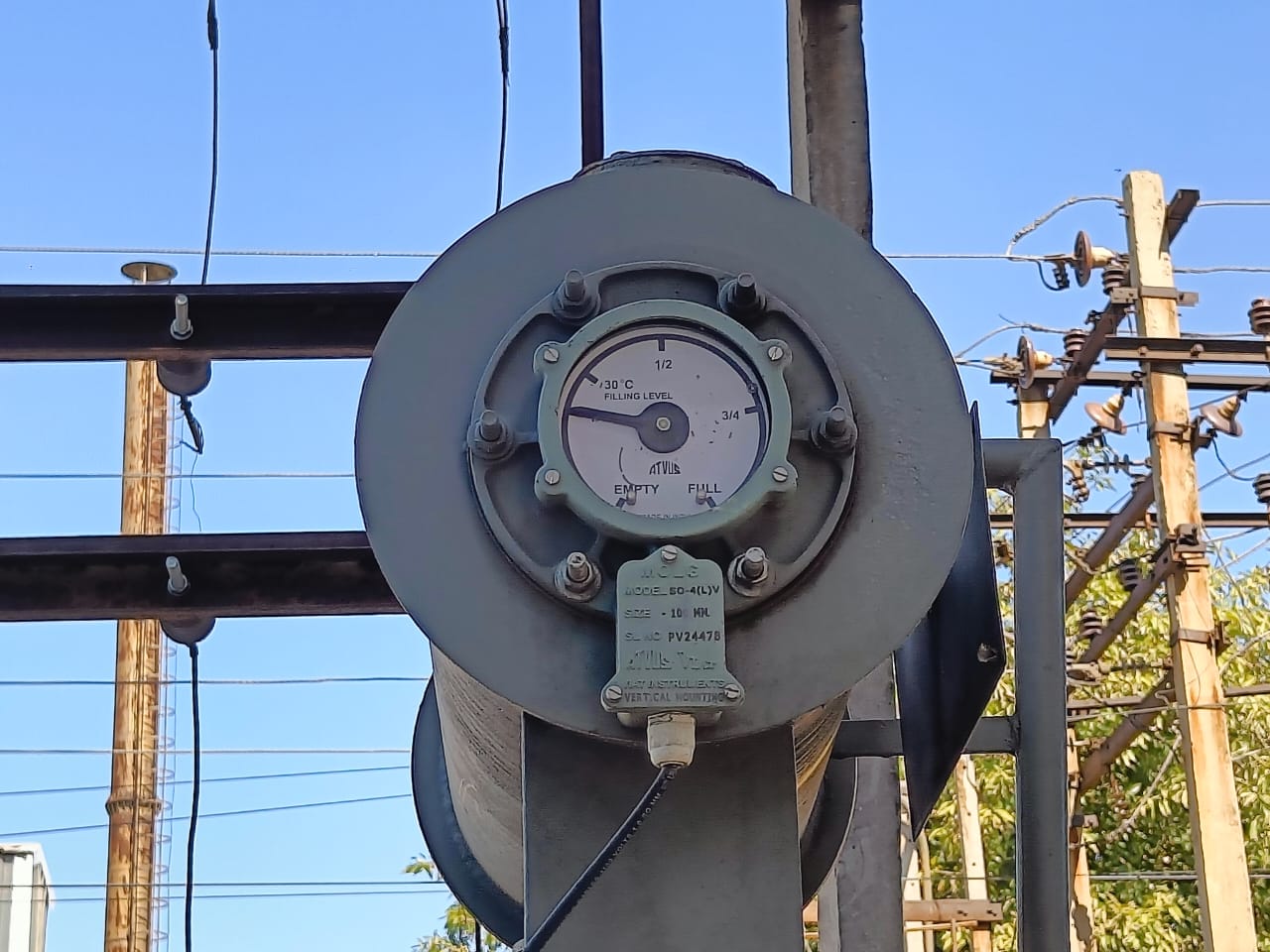 Close-up of an electrical gauge mounted outdoors, with a dial reading “EMPTY” to “FULL” and a clear sky in the background. Power lines and utility poles are visible, similar to those near Elion Technologies’ blower performance testing sites in Uttar Pradesh.