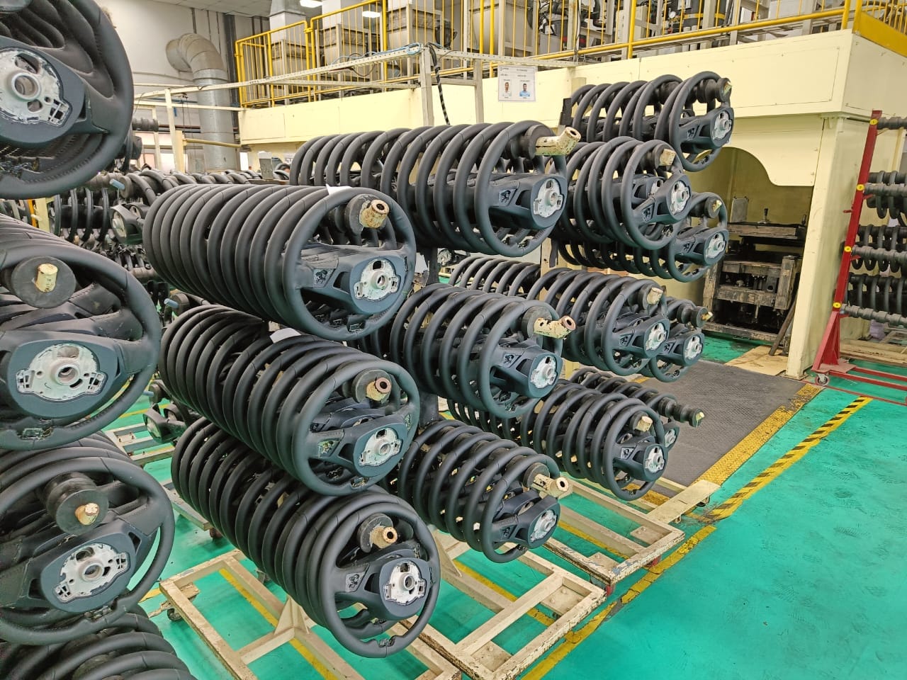 Several stacks of large, coiled metal springs with attached circular components are organized on racks inside an industrial facility, part of a Rewa industrial audit focused on sustainability and Madhya Pradesh water conservation.