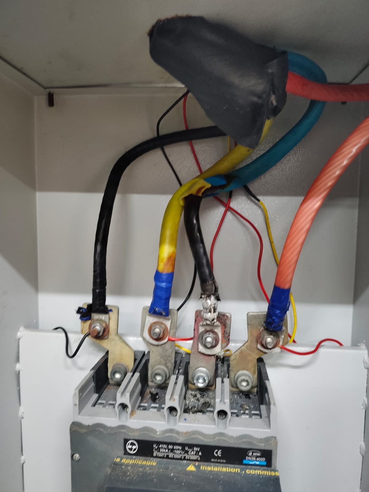 Four thick electrical cables—red, blue, yellow, and black—are connected to metal terminals inside an electrical panel at a Nagpur beverage plant. The setup highlights the importance of industrial electrical safety for routine compliance audits.