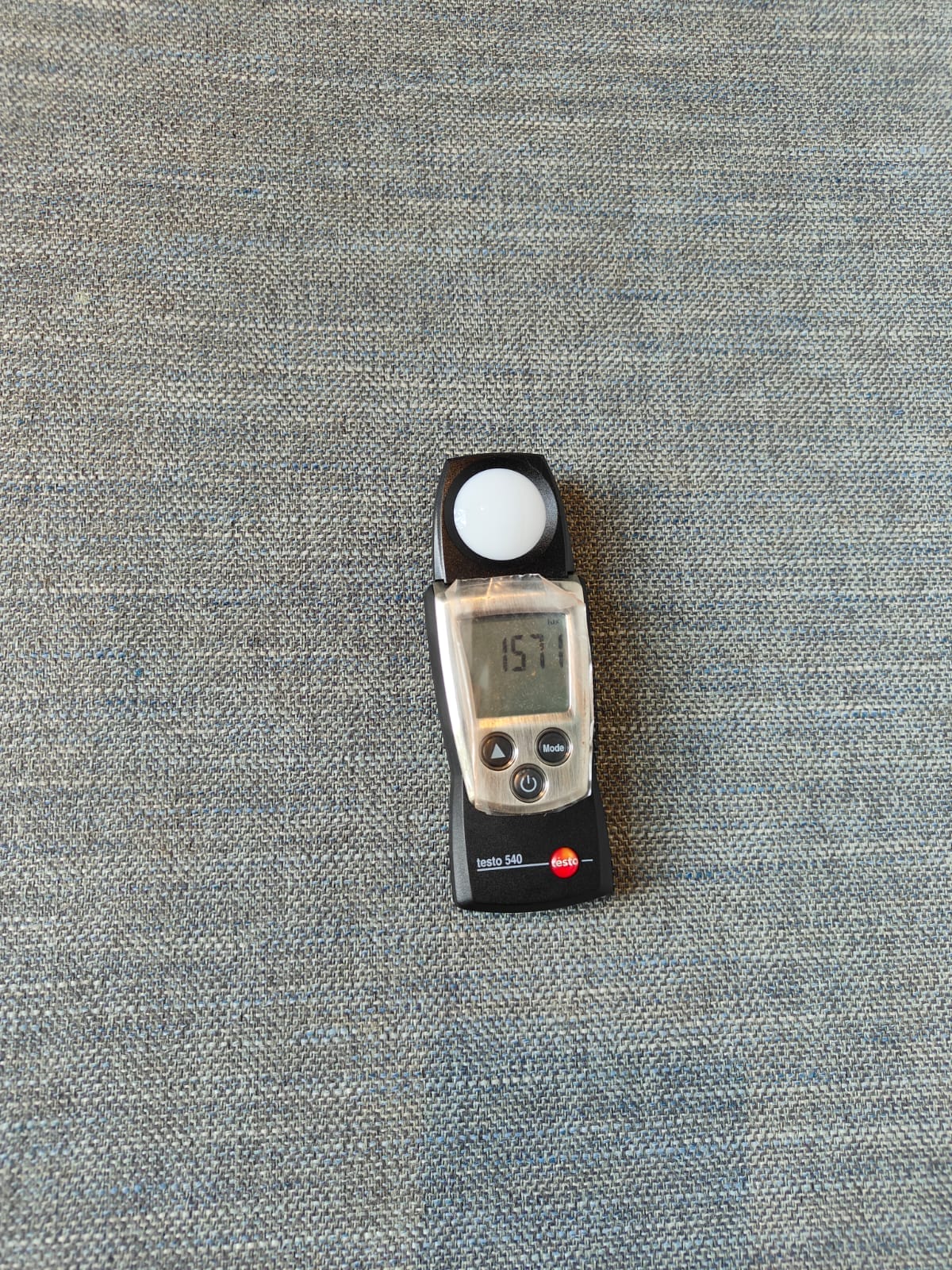 A digital light meter displaying a reading of 1571, placed on a textured gray fabric surface during an Elion water management inspection.