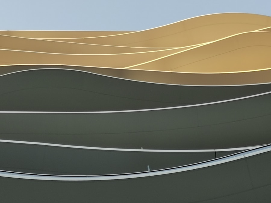Curved, wavy lines in shades of yellow and green form the exterior facade of a modern building against a clear blue sky, creating an abstract and minimalist architectural pattern.