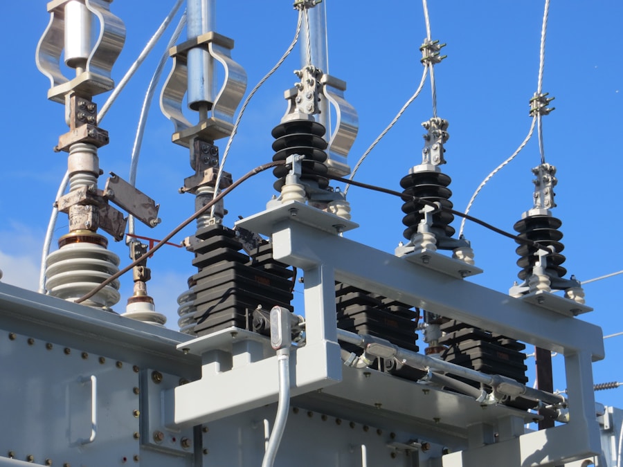 Close-up of electrical power substation equipment with insulators, wires, and metal components against a blue sky background.