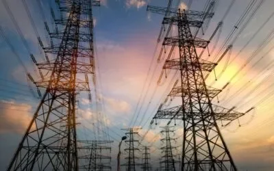 Tall electrical transmission towers with multiple power lines stretch across the sky at sunset, with a colorful background of clouds and fading sunlight—reminders of the importance of regular Energy Audit & Safety Audit for reliable power.
